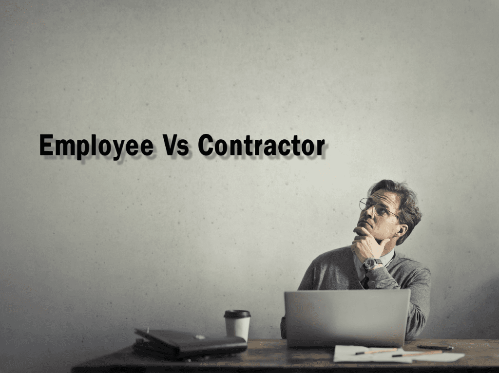 a man sitting at a desk looking up at a sign that says "employee vs contractor"