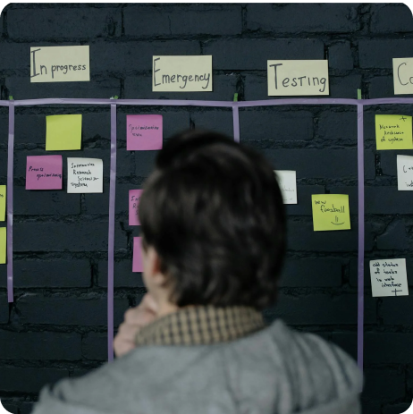 A boss checks a wall with sticky notes and indication of employee progress
