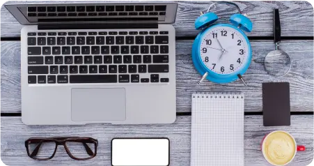 A wooden table displays a laptop, coffee cup, glasses, alarm clock, and various other items, creating a cozy workspace.