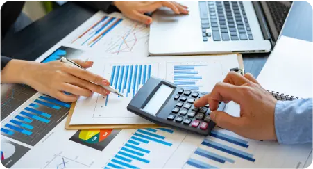 An individual working on business tasks, using a calculator alongside a laptop for efficient calculations.