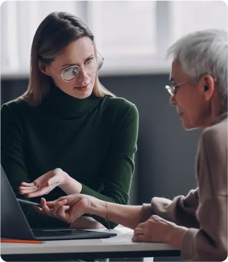 A woman and an older woman engage in conversation while using a laptop, sharing ideas and connecting through technology.