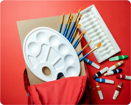 A red bag containing paint brushes, vibrant paint tubes, and a colorful paint palette arranged neatly inside.