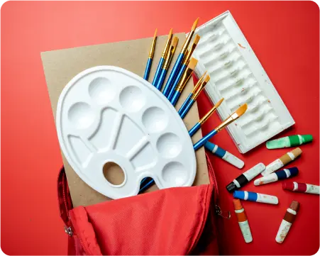 A red bag containing paint brushes, vibrant paint tubes, and a colorful paint palette arranged neatly inside.