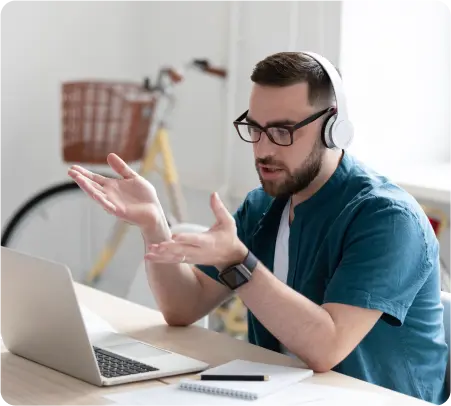 A man with headphones and glasses is seated at a desk, focused on his laptop.