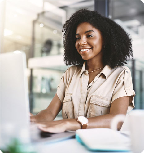 A smiling woman sits at her desk, engaged with her laptop, creating a warm and productive atmosphere.