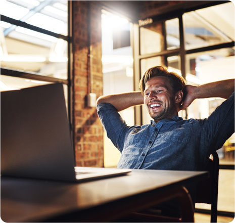 A man at a desk, smiling with his head held high, exuding confidence and positivity in a professional setting.