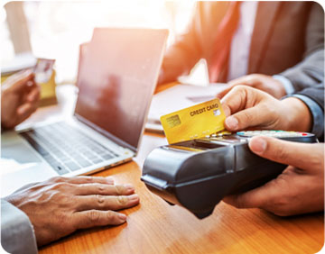 A person holds a credit card in one hand while using a laptop with the other hand, focused on online transactions.