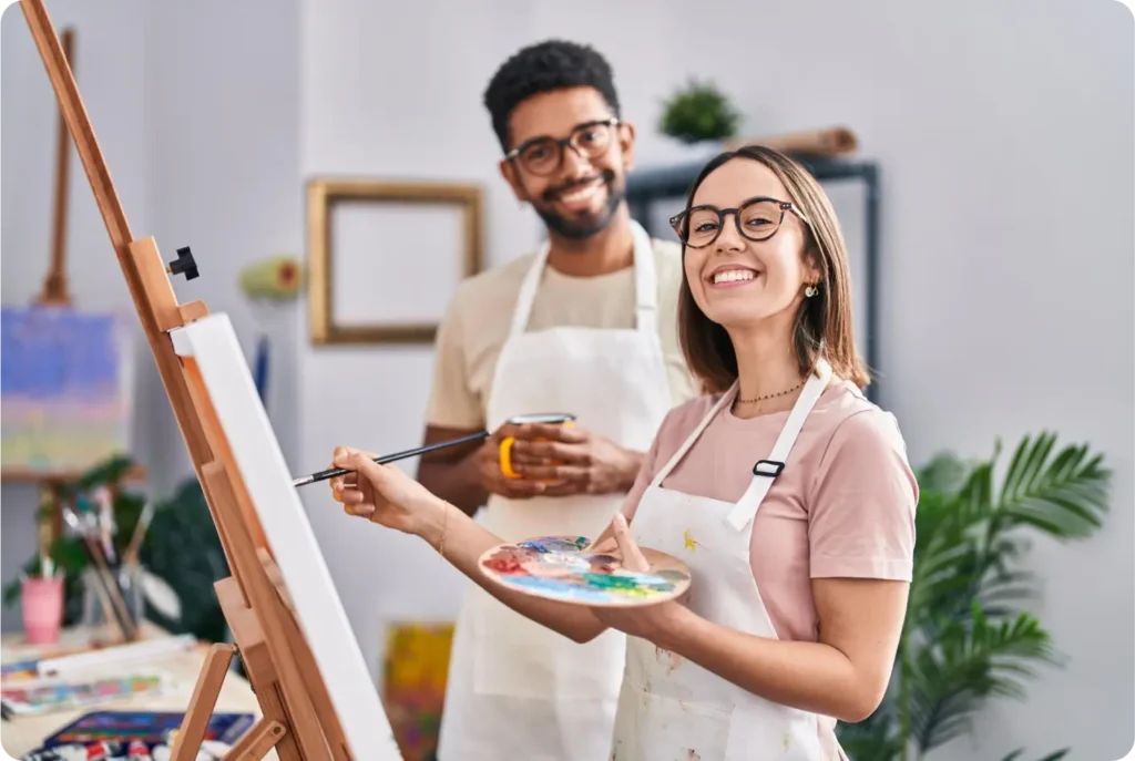 A man and woman are joyfully holding paintbrushes, ready to create art together with vibrant colors.