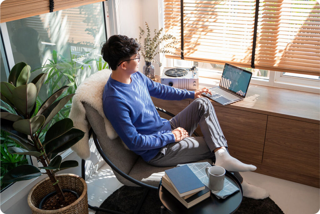 A man seated in a chair, focused on his laptop, engaged in work or leisure activities.